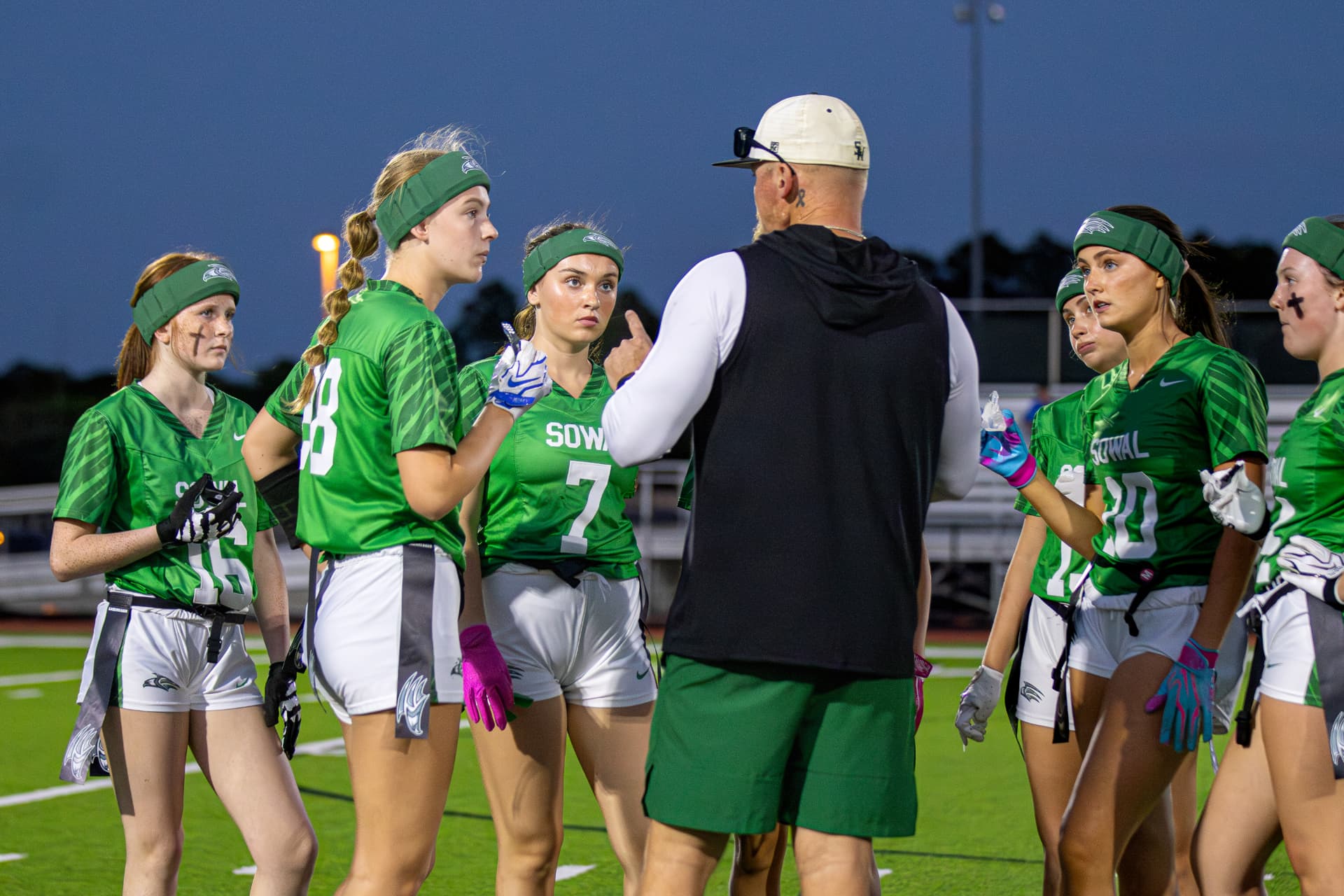 Lady Seahawks huddle with their coach under the lights